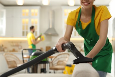 Photo of Professional janitor in uniform vacuuming sofa indoors, closeup. Space for text