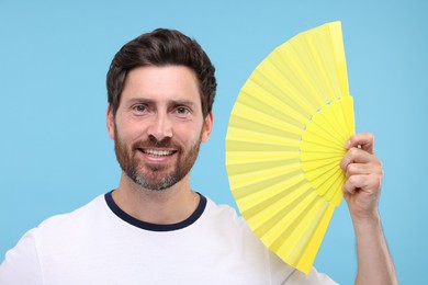 Happy man holding hand fan on light blue background