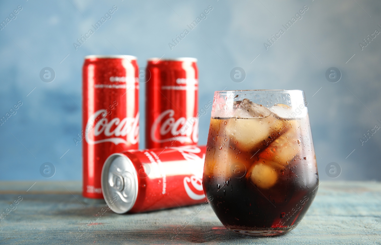 Photo of MYKOLAIV, UKRAINE - NOVEMBER 15, 2018: Glass and cans with Coca Cola on table against color background