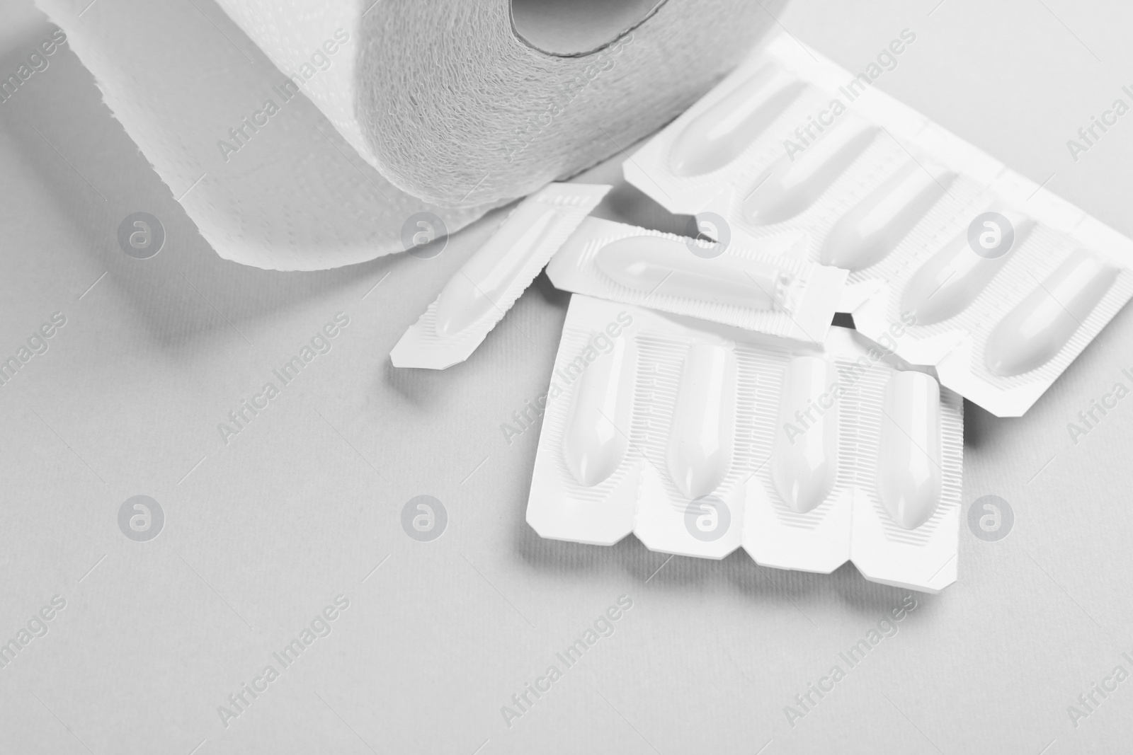 Photo of Suppositories and toilet paper on light background. Hemorrhoid treatment