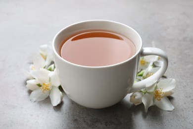 Photo of Cup of aromatic jasmine tea and fresh flowers on grey table