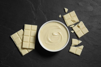 Photo of Tasty white chocolate paste in bowl and pieces on black table, top view