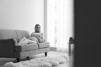 Beautiful pregnant woman resting on sofa at home, black and white effect