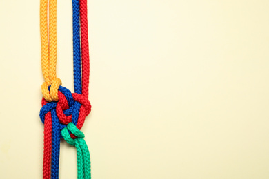 Top view of colorful ropes tied together on beige background, space for text. Unity concept