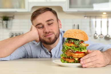 Photo of Young hungry man and huge burger on table