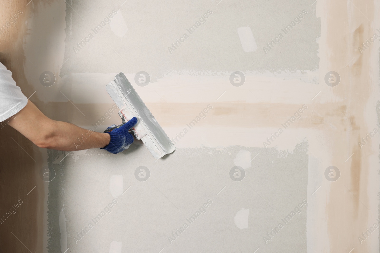 Photo of Worker plastering wall with putty knife indoors, closeup. Space for text