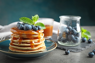 Photo of Delicious pancakes with fresh blueberries and syrup on grey table