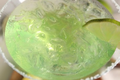Delicious Margarita cocktail with ice cubes in glass and lime, closeup