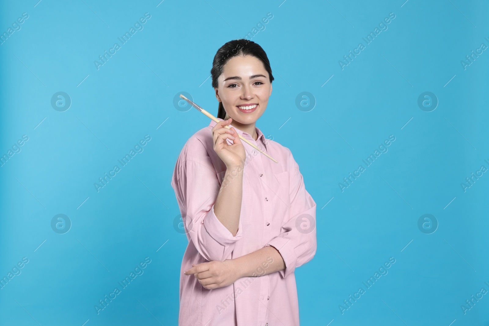 Photo of Woman with paintbrush on light blue background. Young artist