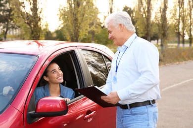 Instructor near woman in car, outdoors. Passing driving license exam