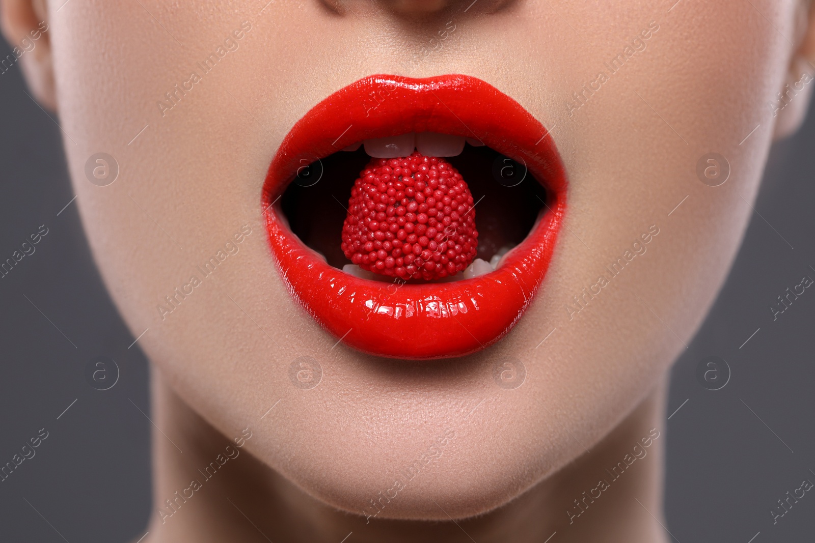 Photo of Young woman with red lips makeup eating candy on grey background, closeup