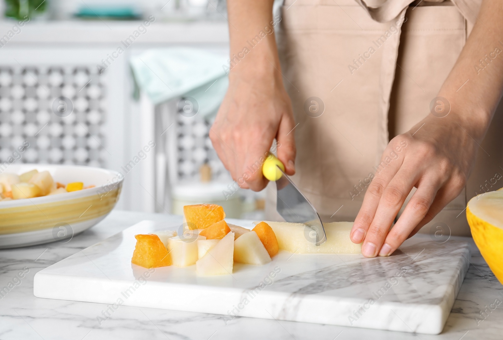 Photo of Woman slicing fresh ripe melon on light table