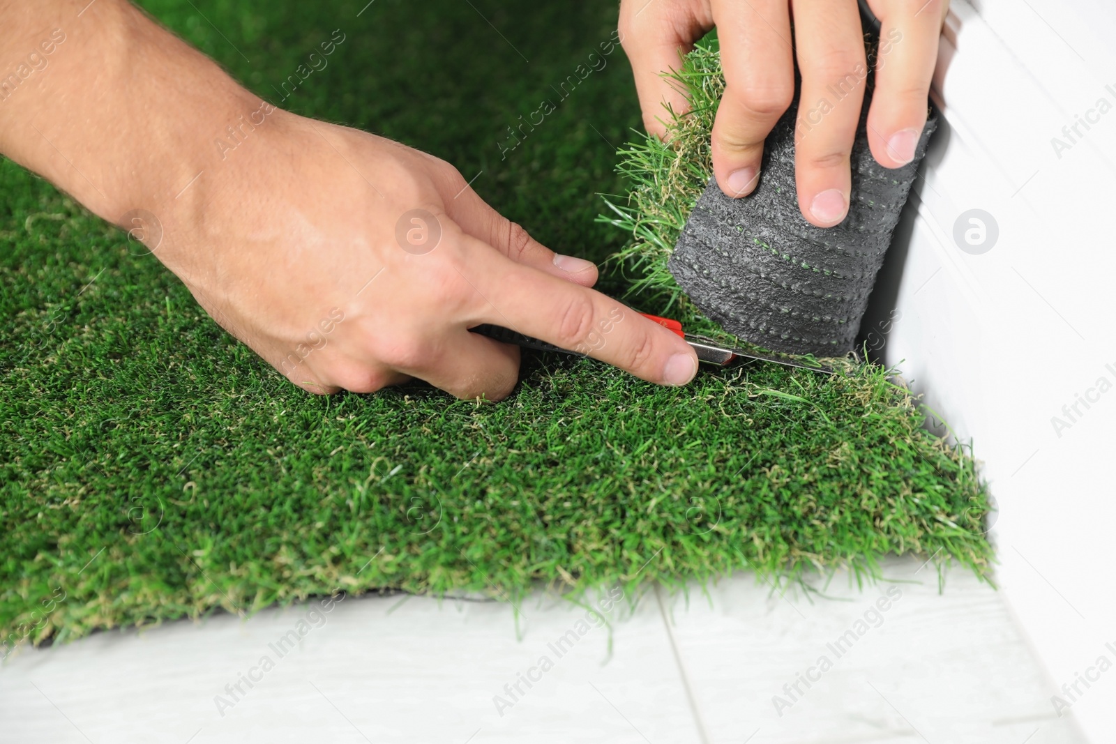 Photo of Man cutting artificial grass carpet indoors, closeup