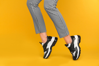 Woman wearing stylish sneakers on yellow background, closeup