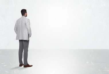 Image of Man standing in front of light marble wall, back view. Space for text