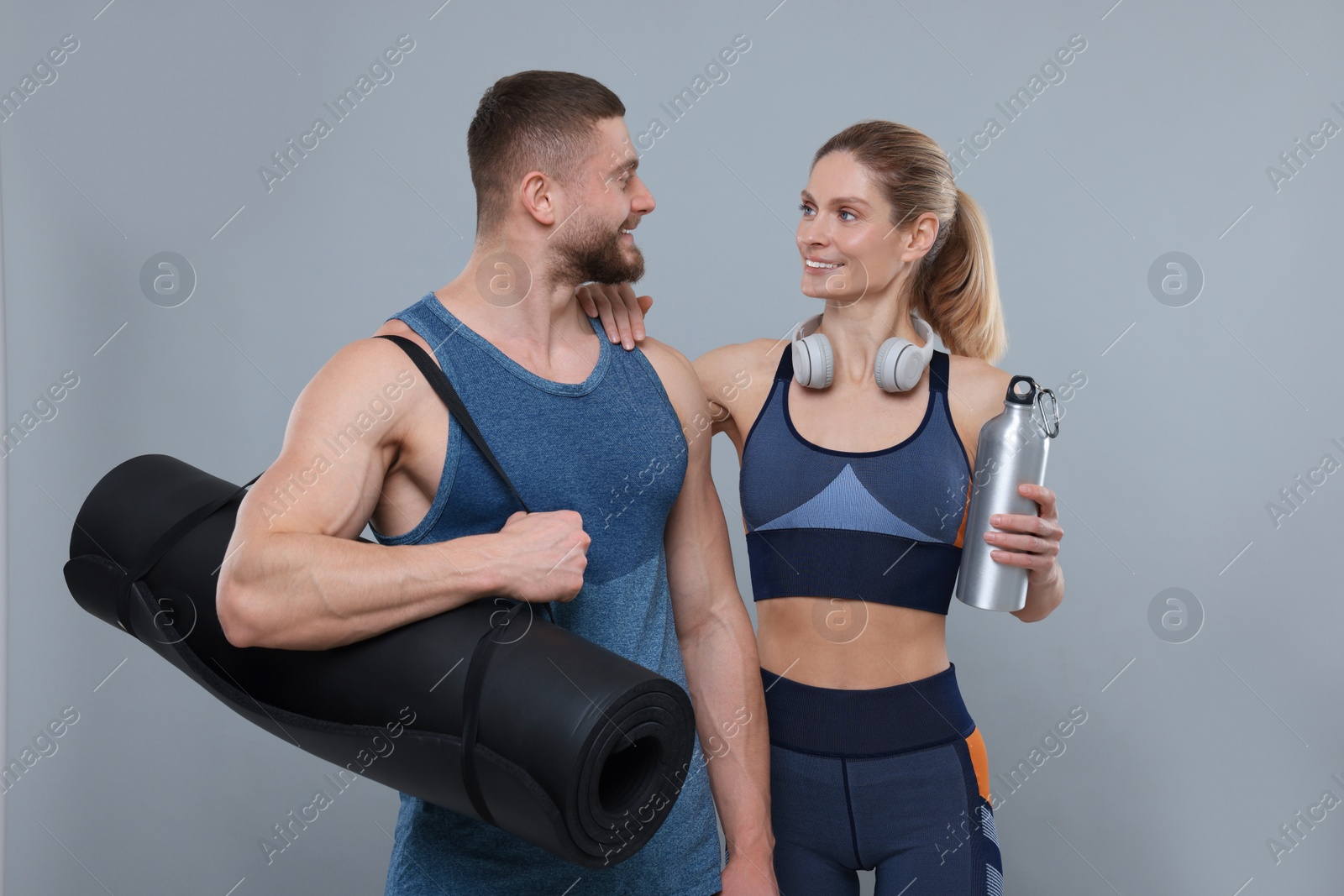 Photo of Athletic people with headphones, thermo bottle and fitness mat on grey background