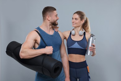 Athletic people with headphones, thermo bottle and fitness mat on grey background