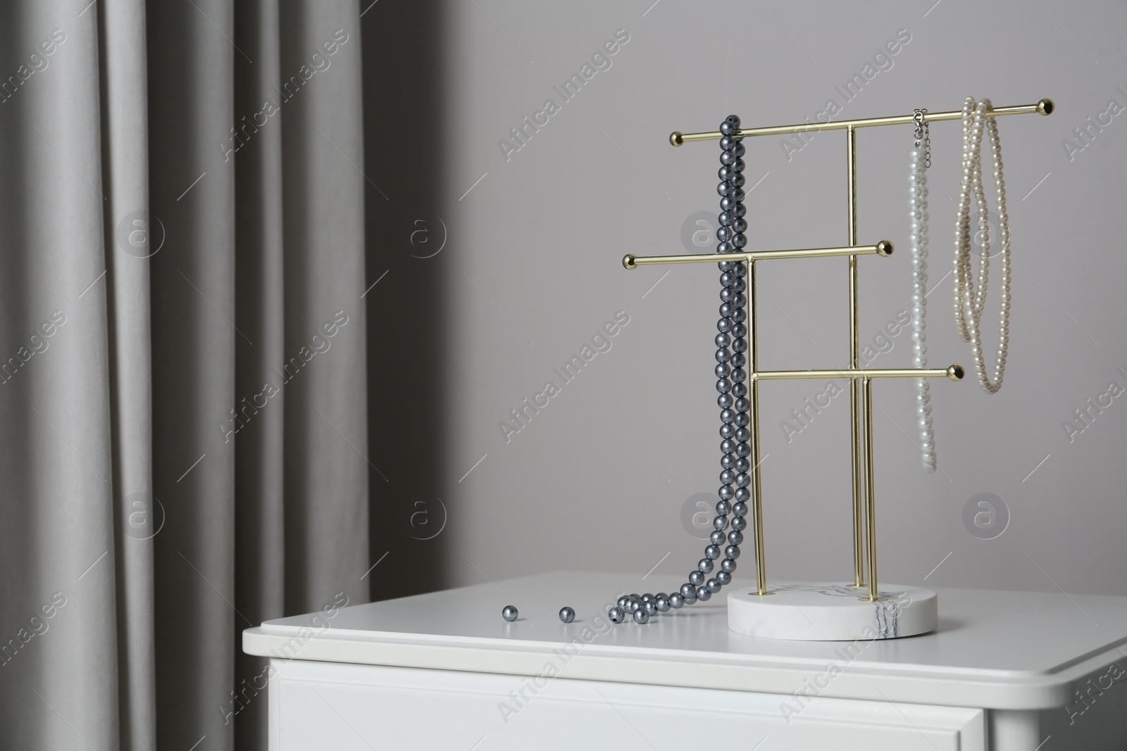 Photo of Interior element. Holder with set of luxurious jewelry on white table. Space for text