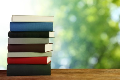 Image of Many stacked hardcover books on wooden table against blurred background, space for text
