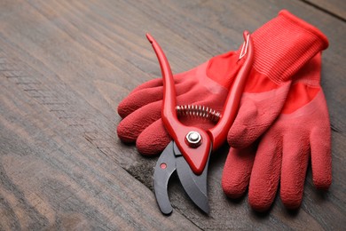 Photo of Pair of red gardening gloves and secateurs on wooden table, space for text