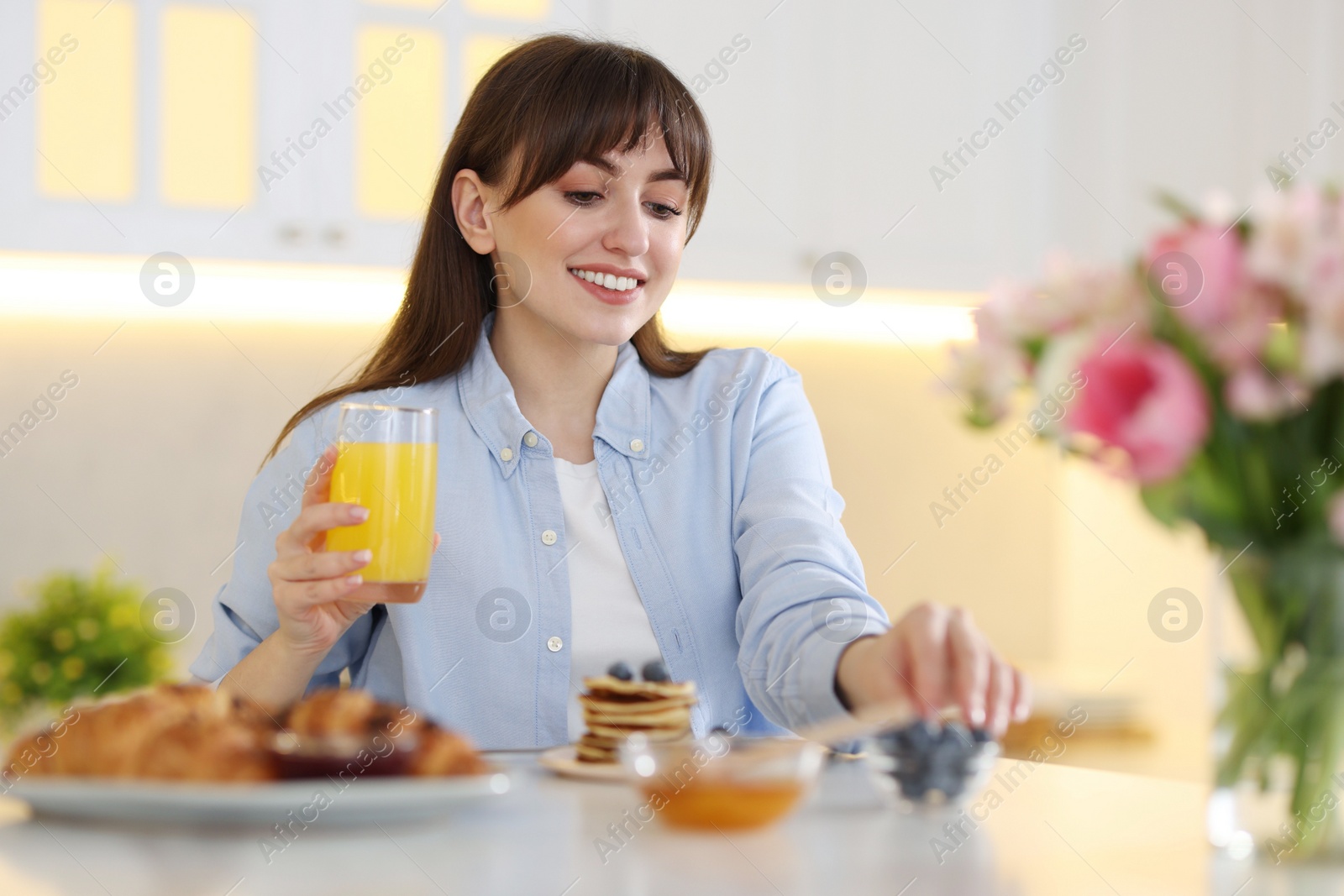 Photo of Smiling woman with glass of juice having breakfast at home