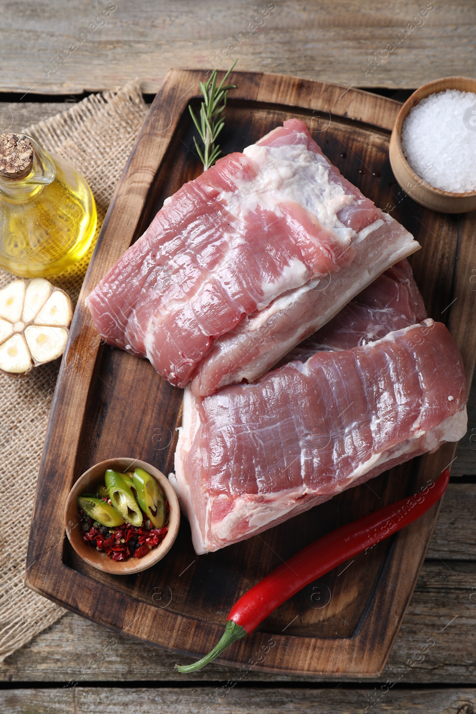 Photo of Pieces of raw pork belly, oil, garlic, salt and spices on wooden table, flat lay