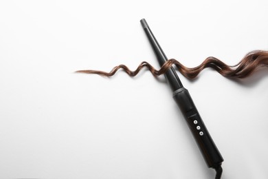 Photo of Modern clipless curling iron and brown hair lock on white background