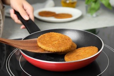 Photo of Woman cooking breaded cutlets in frying pan on stove, closeup