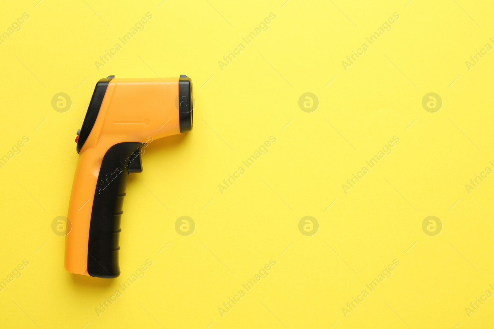 Photo of Infrared thermometer on yellow background, top view with space for text. Checking temperature during Covid-19 pandemic