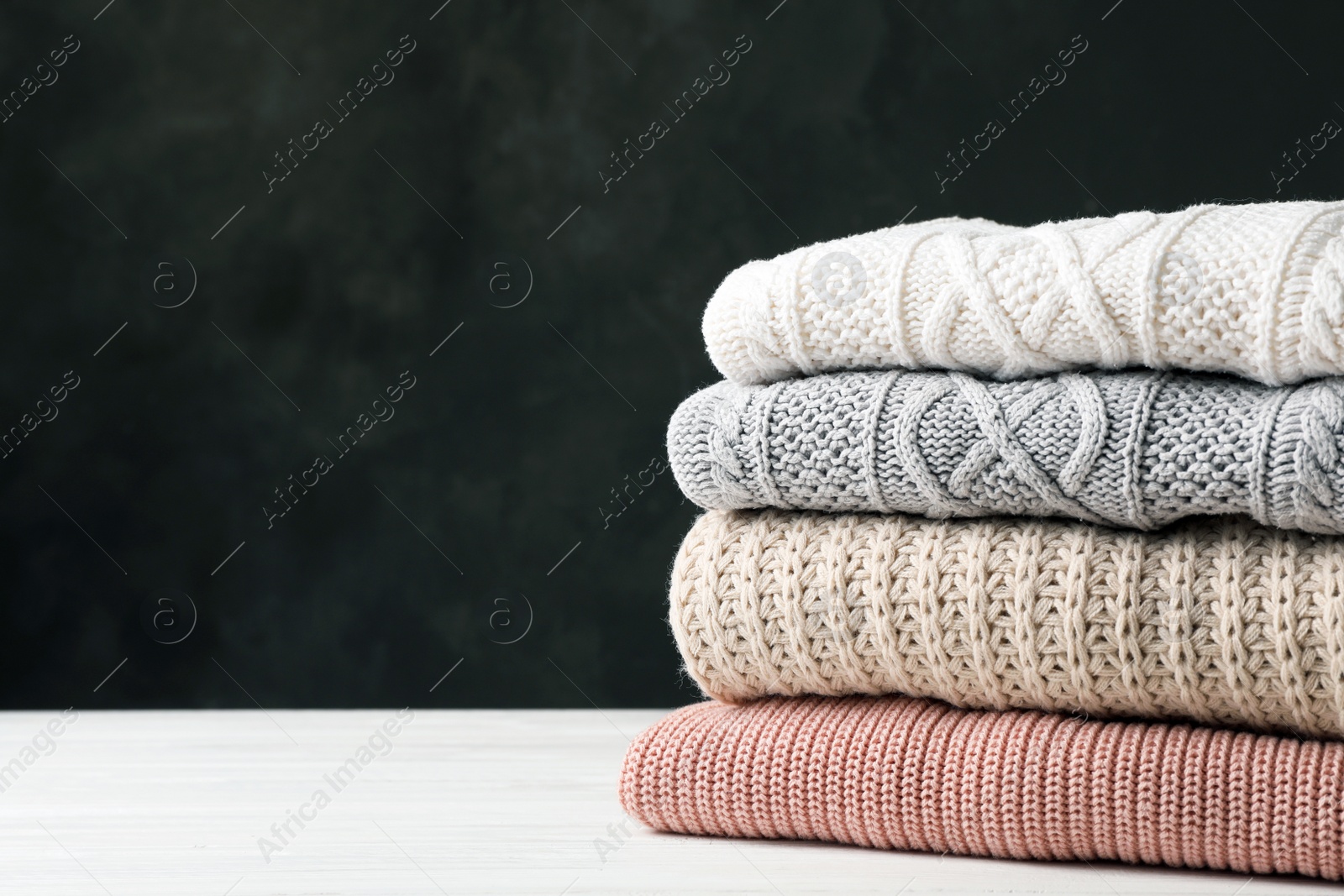 Photo of Stack of folded knitted sweaters on table. Space for text