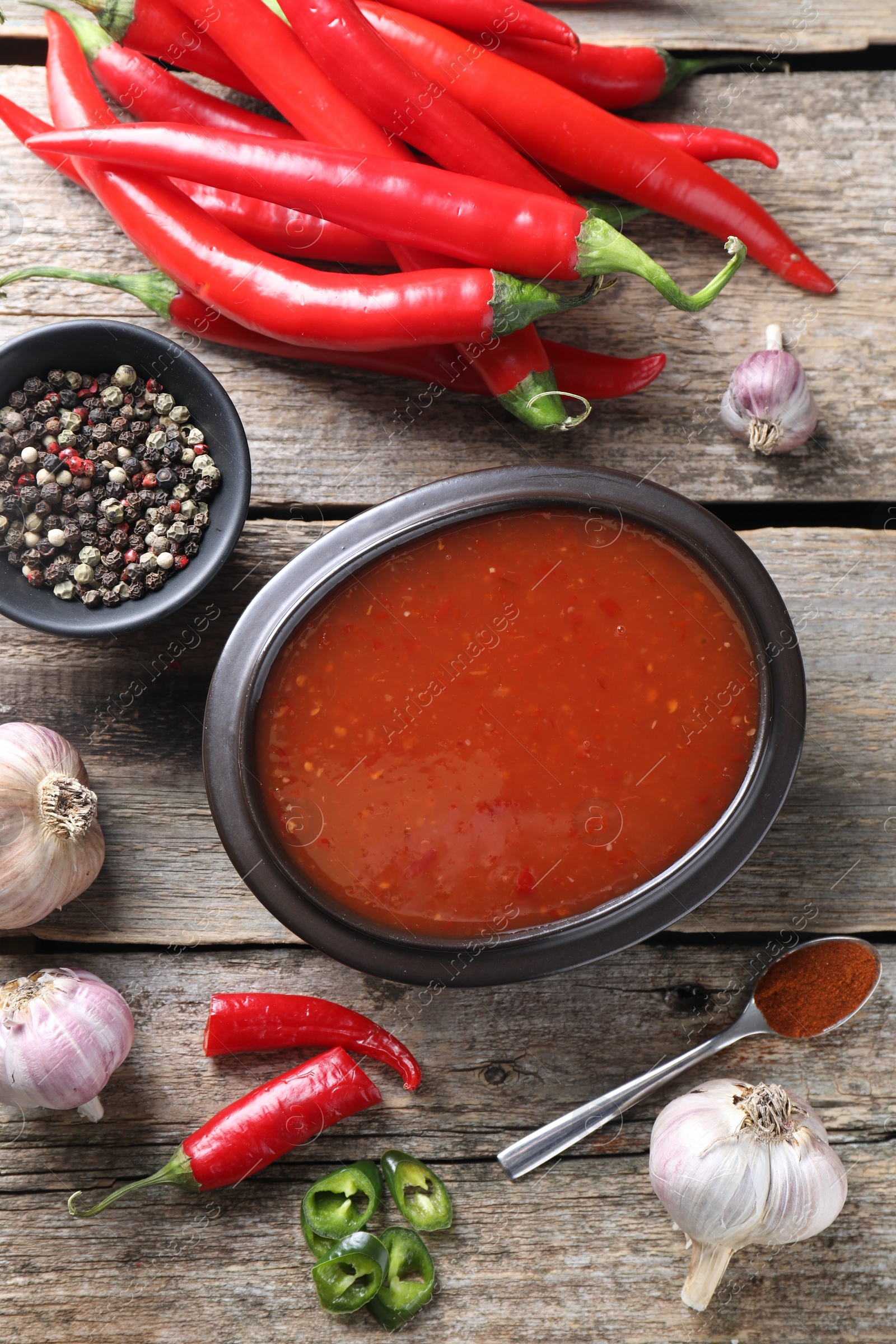 Photo of Spicy chili sauce in bowl and ingredients on wooden table, flat lay