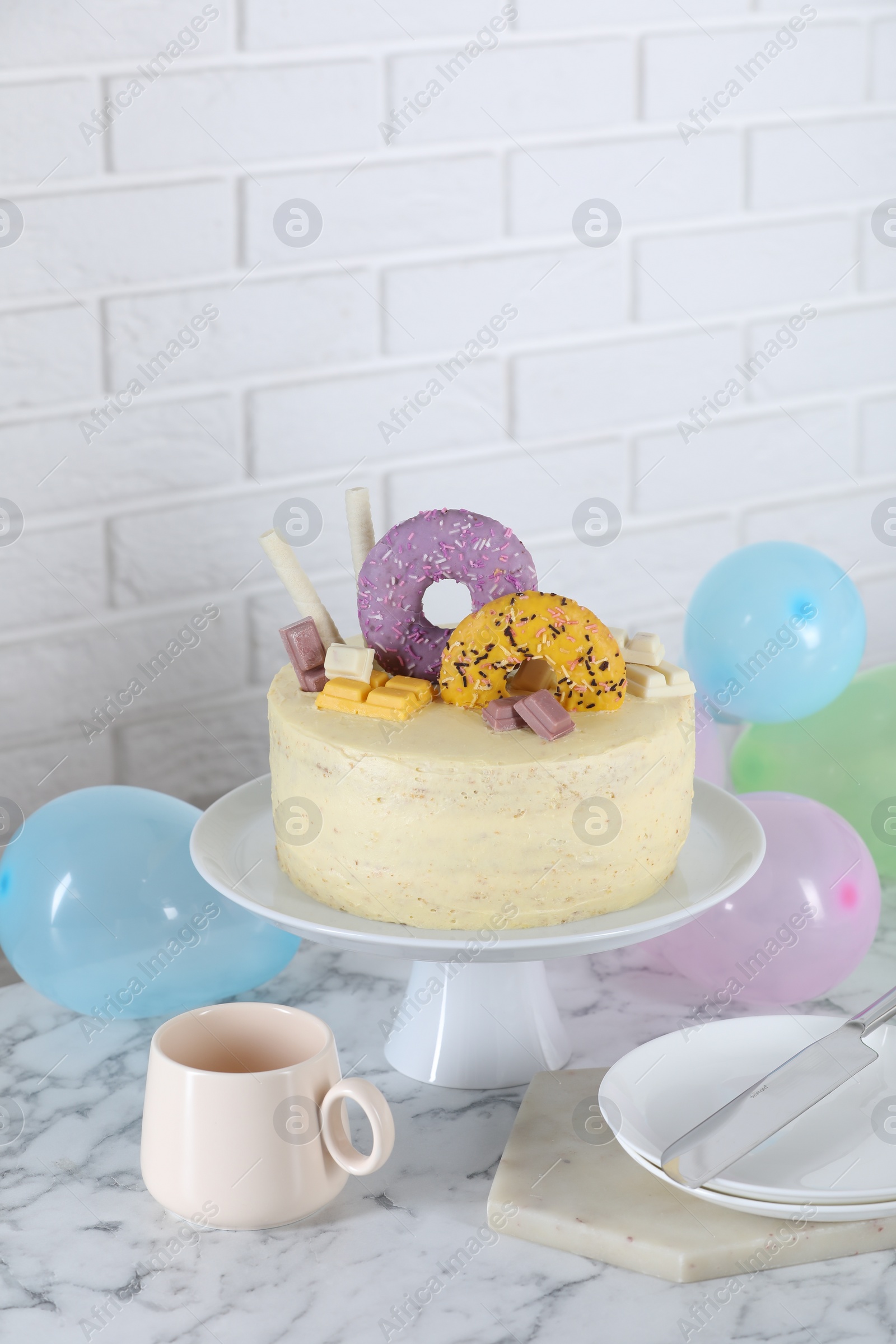 Photo of Delicious cake decorated with sweets, tableware and balloons on white marble table, space for text