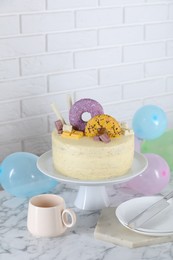 Photo of Delicious cake decorated with sweets, tableware and balloons on white marble table, space for text
