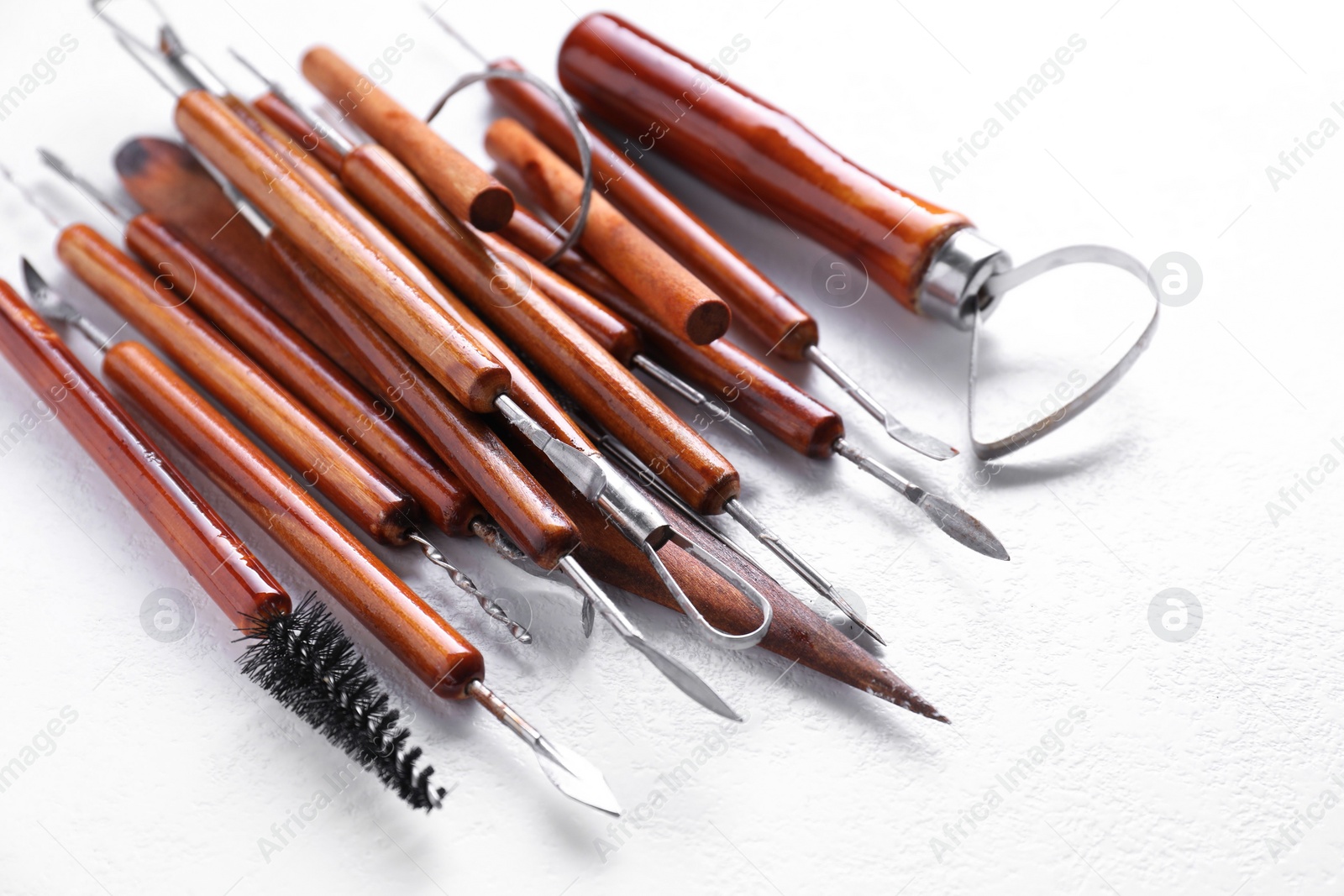 Photo of Set of different clay crafting tools on white textured table, closeup