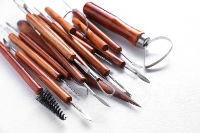 Set of different clay crafting tools on white textured table, closeup