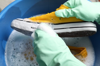 Woman with gloves and sponge cleaning stylish sneakers in wash basin, top view