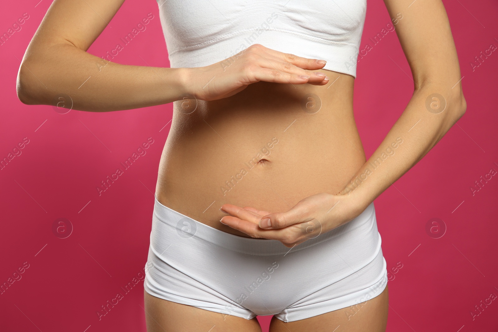 Photo of Woman holding hands near belly against pink background, closeup