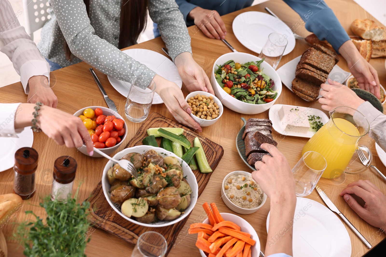 Photo of Friends eating vegetarian food at wooden table indoors, closeup