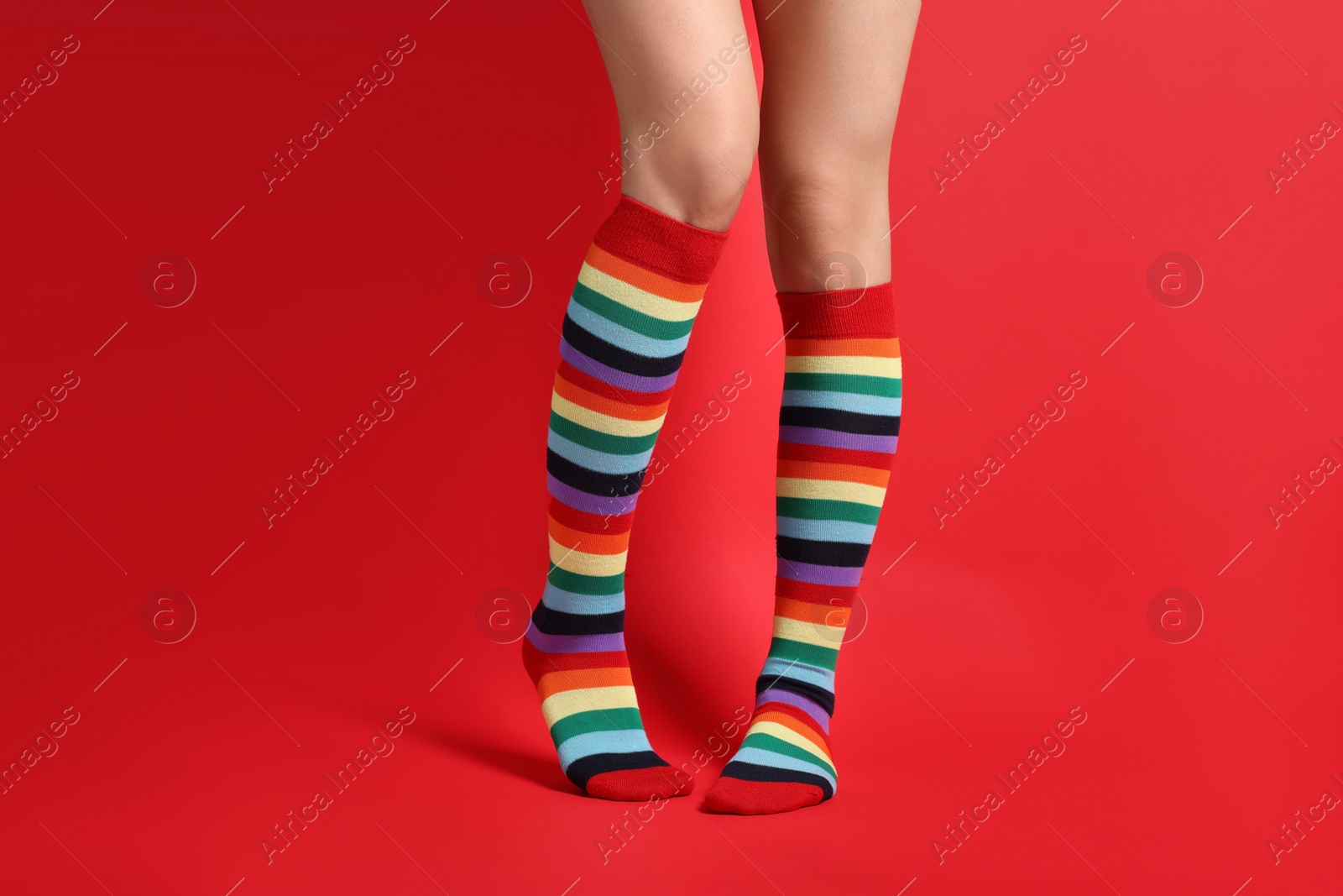 Photo of Woman in stylish rainbow socks on red background, closeup