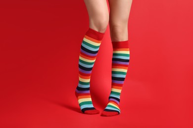 Photo of Woman in stylish rainbow socks on red background, closeup