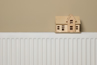 Photo of Modern radiator with wooden house near beige wall indoors. Winter heating efficiency