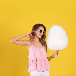 Happy young woman with cotton candy on yellow background