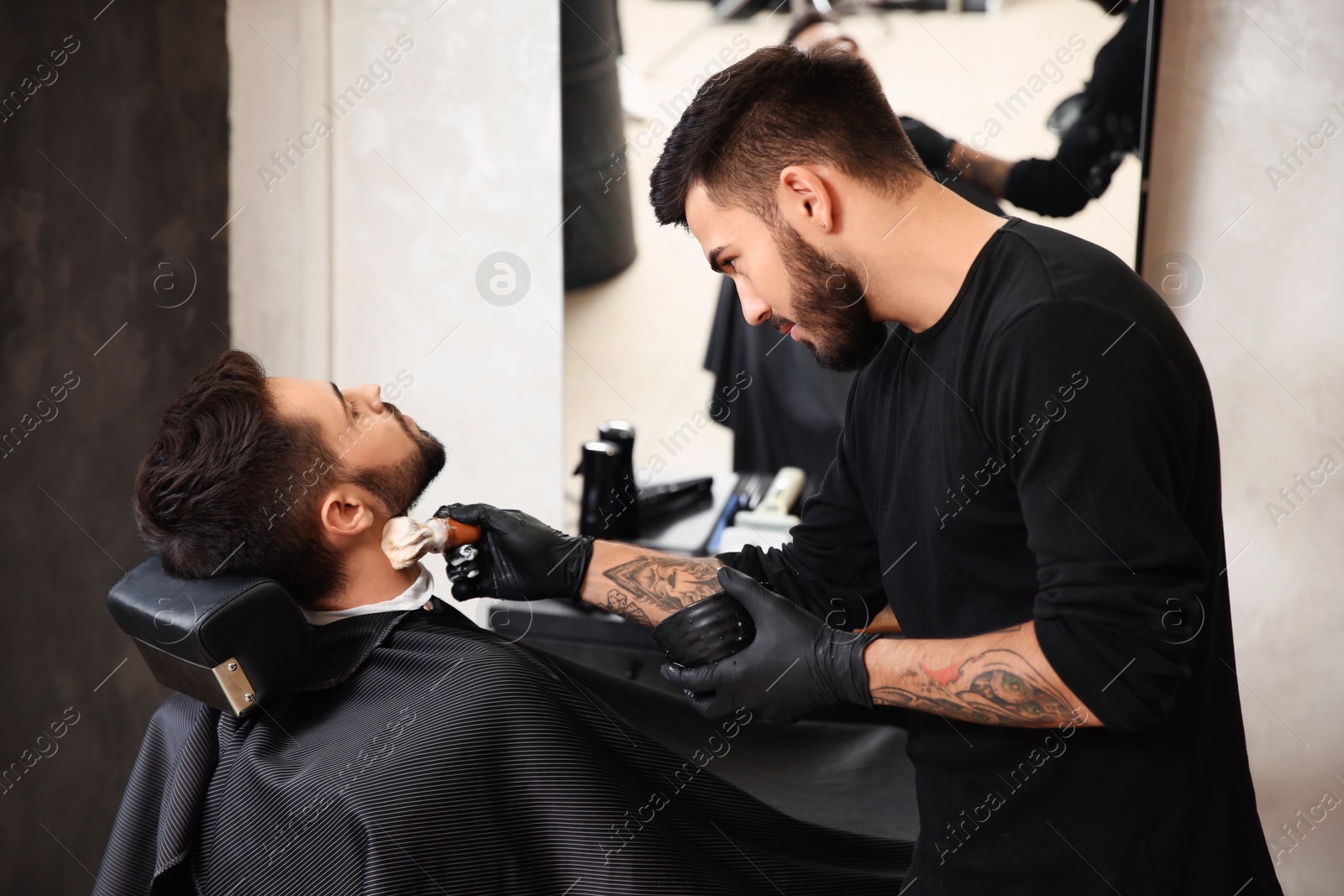 Photo of Professional hairdresser applying shaving foam onto client's skin in barbershop