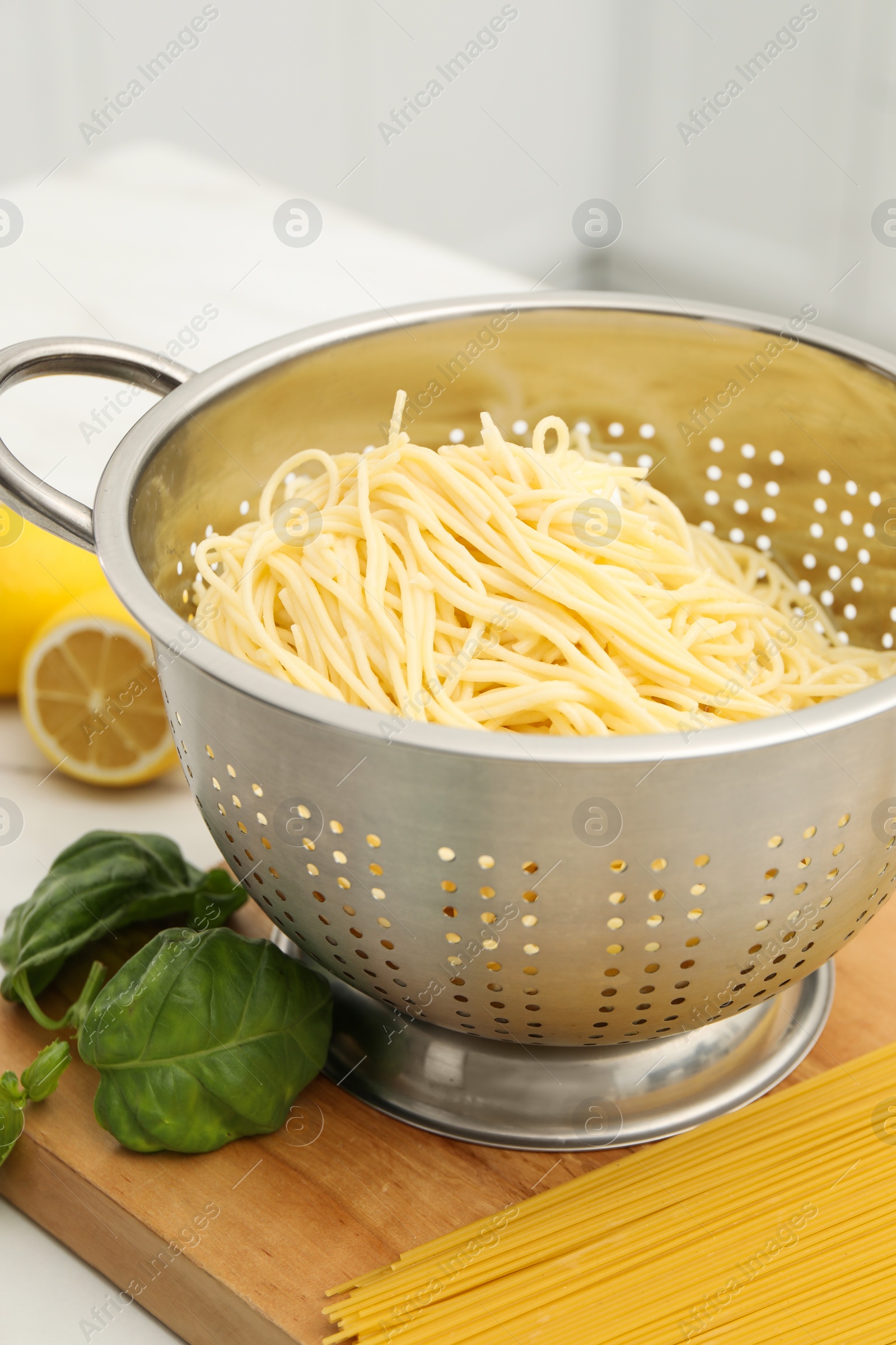 Photo of Cooked pasta in metal colander and products on table, closeup