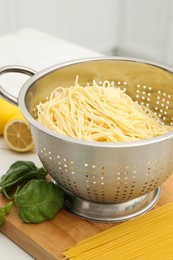 Cooked pasta in metal colander and products on table, closeup