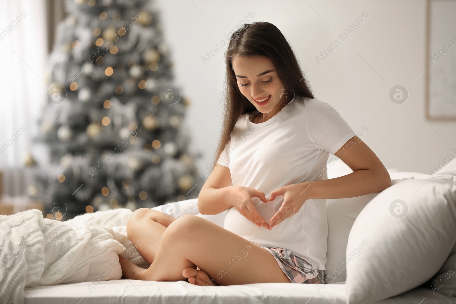 Photo of Happy pregnant woman on bed in room decorated for Christmas. Expecting baby