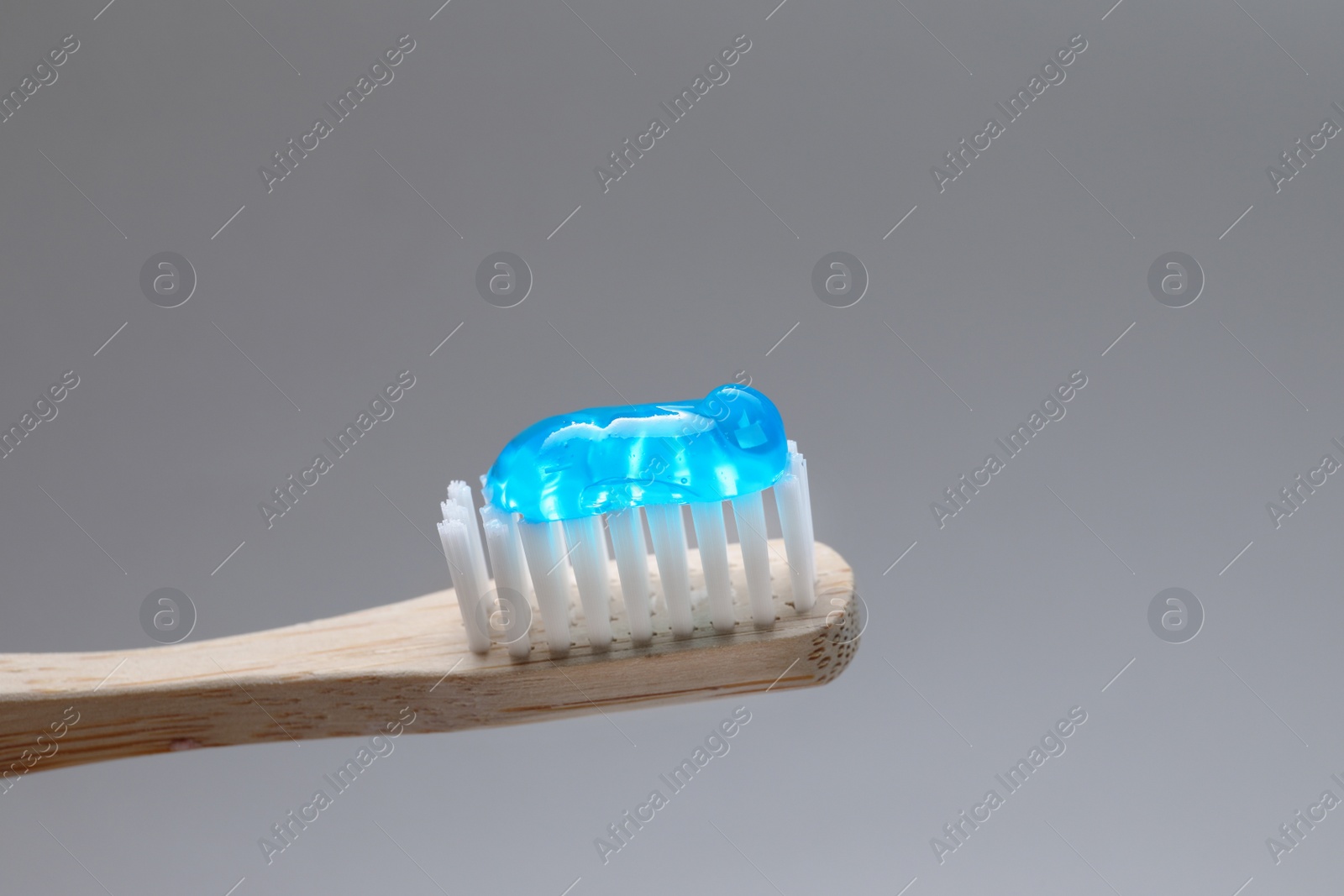 Photo of Wooden brush with toothpaste on grey background, closeup