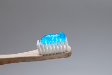 Photo of Wooden brush with toothpaste on grey background, closeup