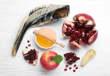 Photo of Honey, pomegranate, apples and shofar on white wooden table, flat lay. Rosh Hashana holiday