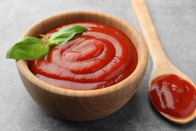 Photo of Bowl and spoon of tasty ketchup with basil on light grey table, closeup